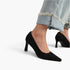 Black pointed-toe high-heel pumps worn with light-wash frayed denim jeans, shown on a model against a clean white background.