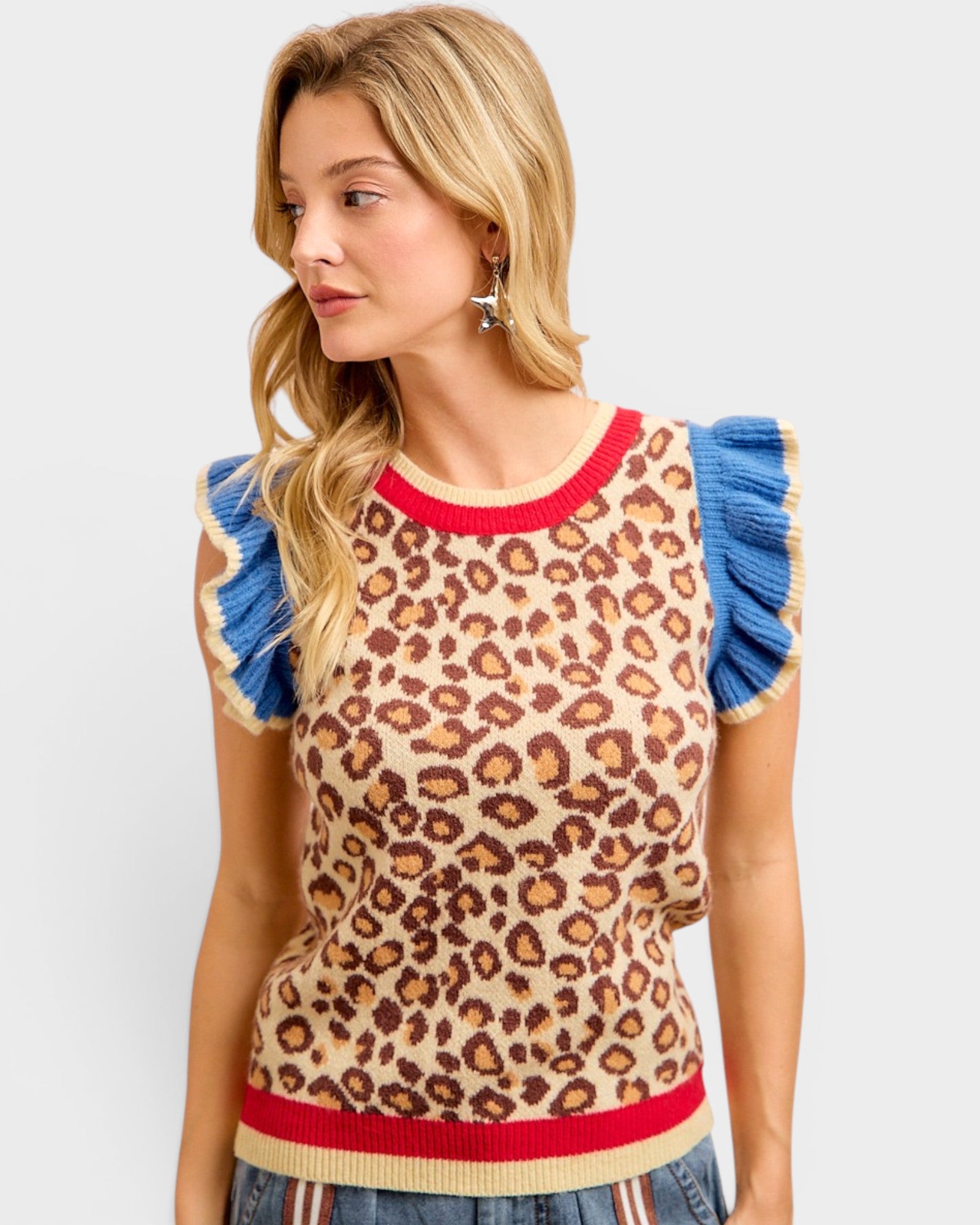 Woman wearing a leopard print sleeveless top with blue ruffled sleeves and red trim on a light gray background.