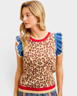 Woman wearing a leopard print sleeveless top with blue ruffled sleeves and red trim on a light gray background.