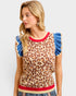 Woman wearing a leopard print sleeveless top with blue ruffled sleeves and red trim on a light gray background.