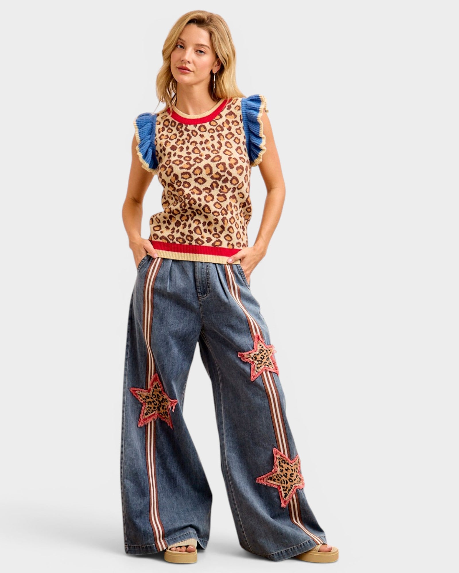 Woman wearing a leopard print top with ruffled sleeves and denim pants with star designs on a white background