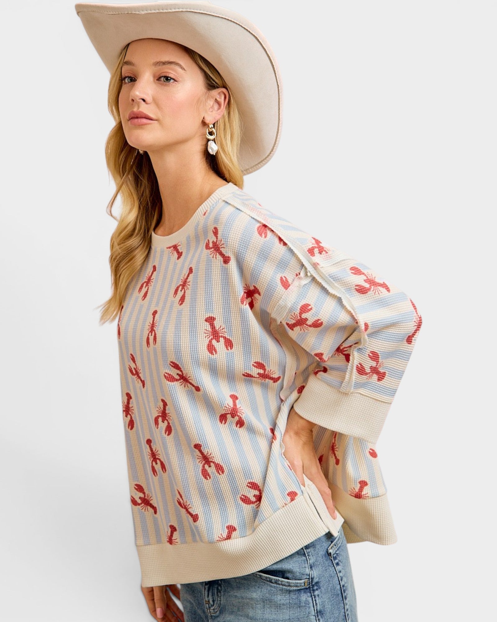 Woman wearing a sweater with lobster pattern and a wide-brimmed hat on a white background
