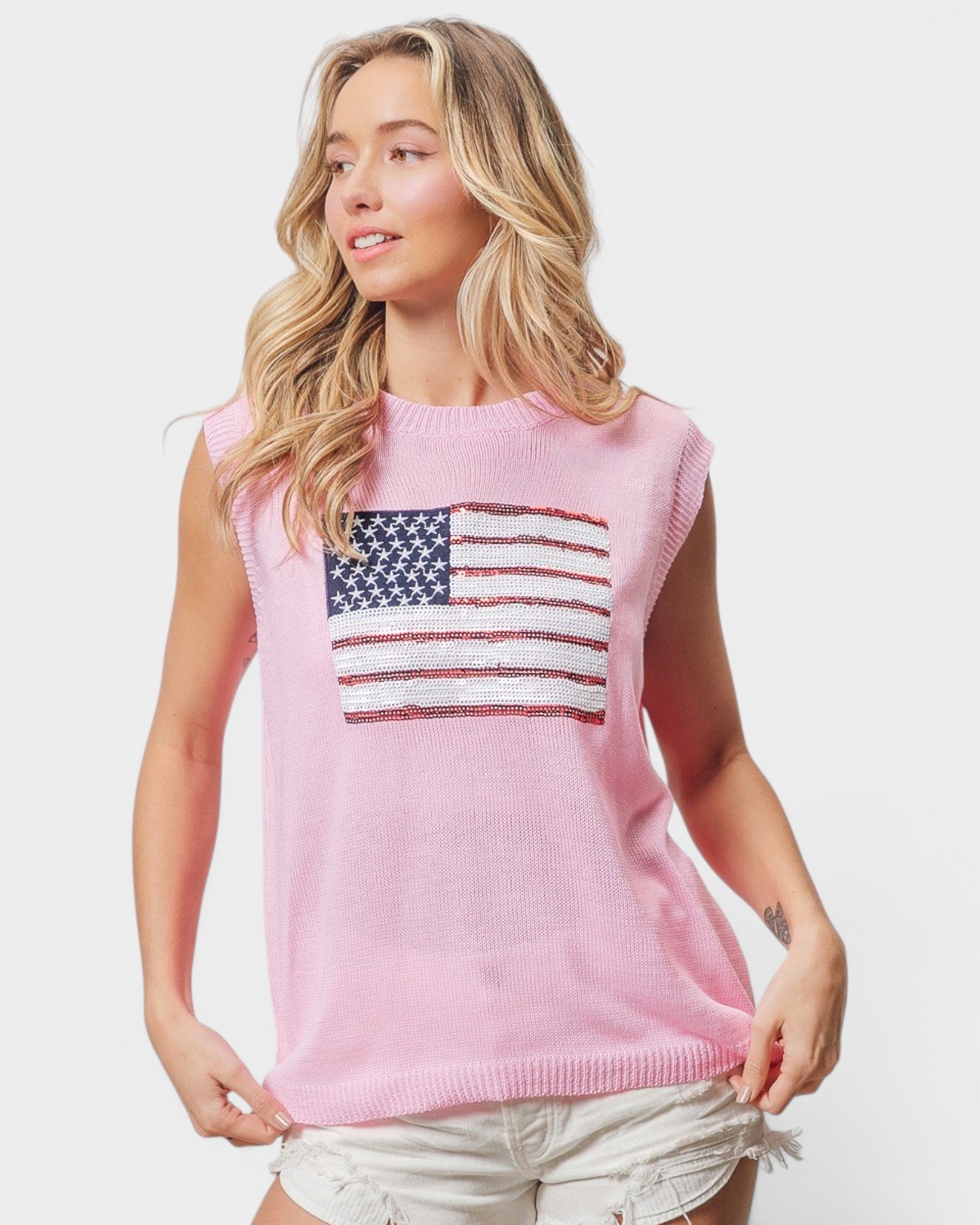 Woman wearing a pink sleeveless sweater with an American flag design on a white background