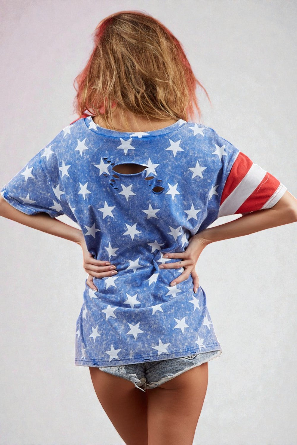 Person wearing a blue star-patterned t-shirt with American flag sleeves on a plain background
