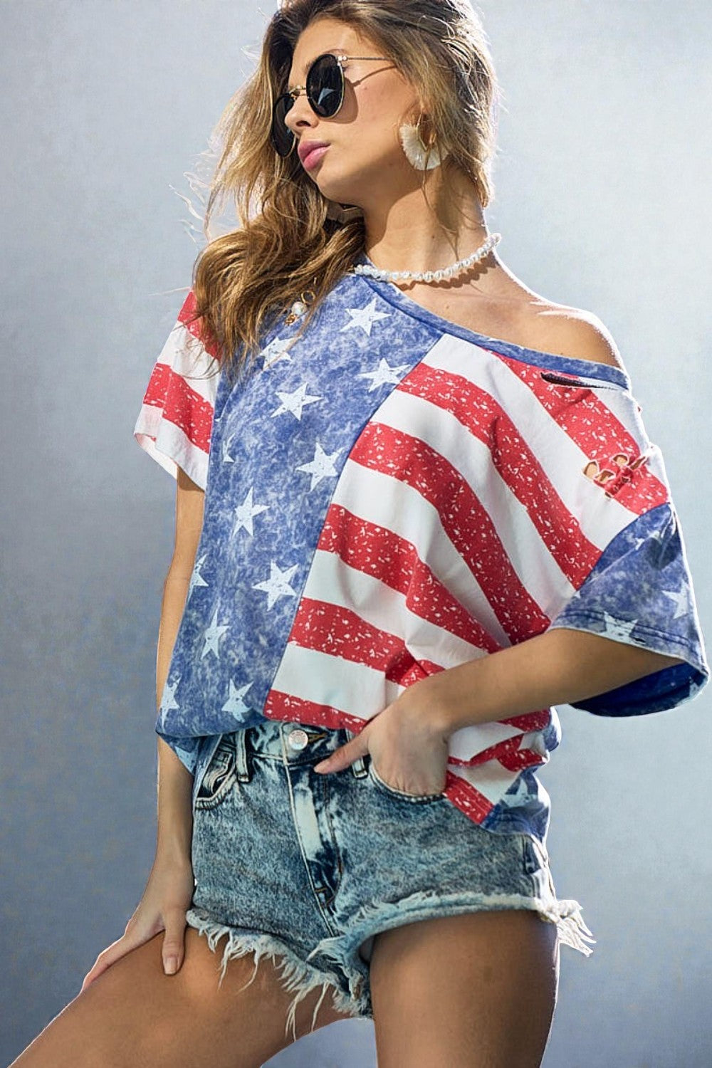 Woman wearing a colorful off-shoulder top with a pattern resembling the American flag against a gray background.