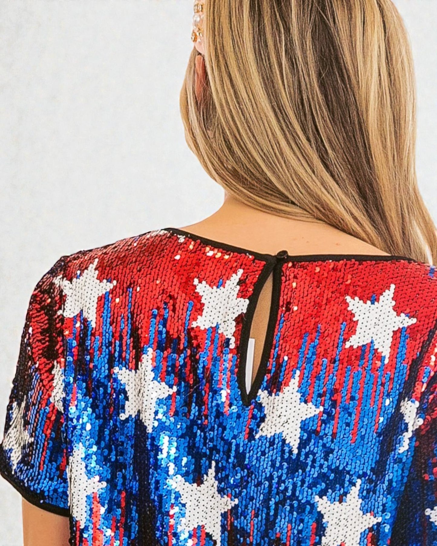 Person wearing a sequin top with star and stripe pattern on a plain background
