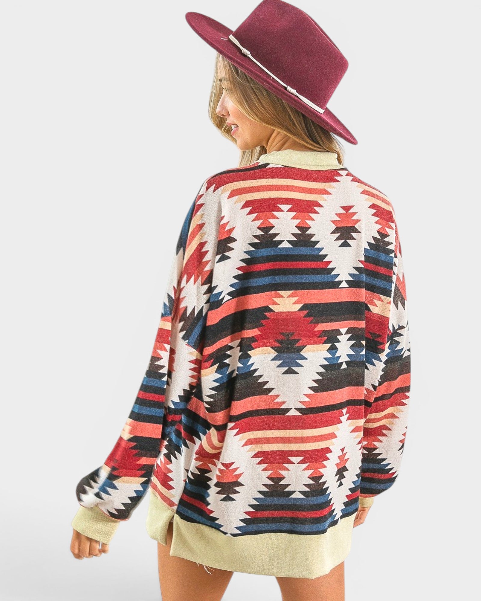 Person wearing a colorful patterned sweater and burgundy hat on a white background
