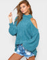 Woman wearing a teal sweater and denim shorts on a plain background