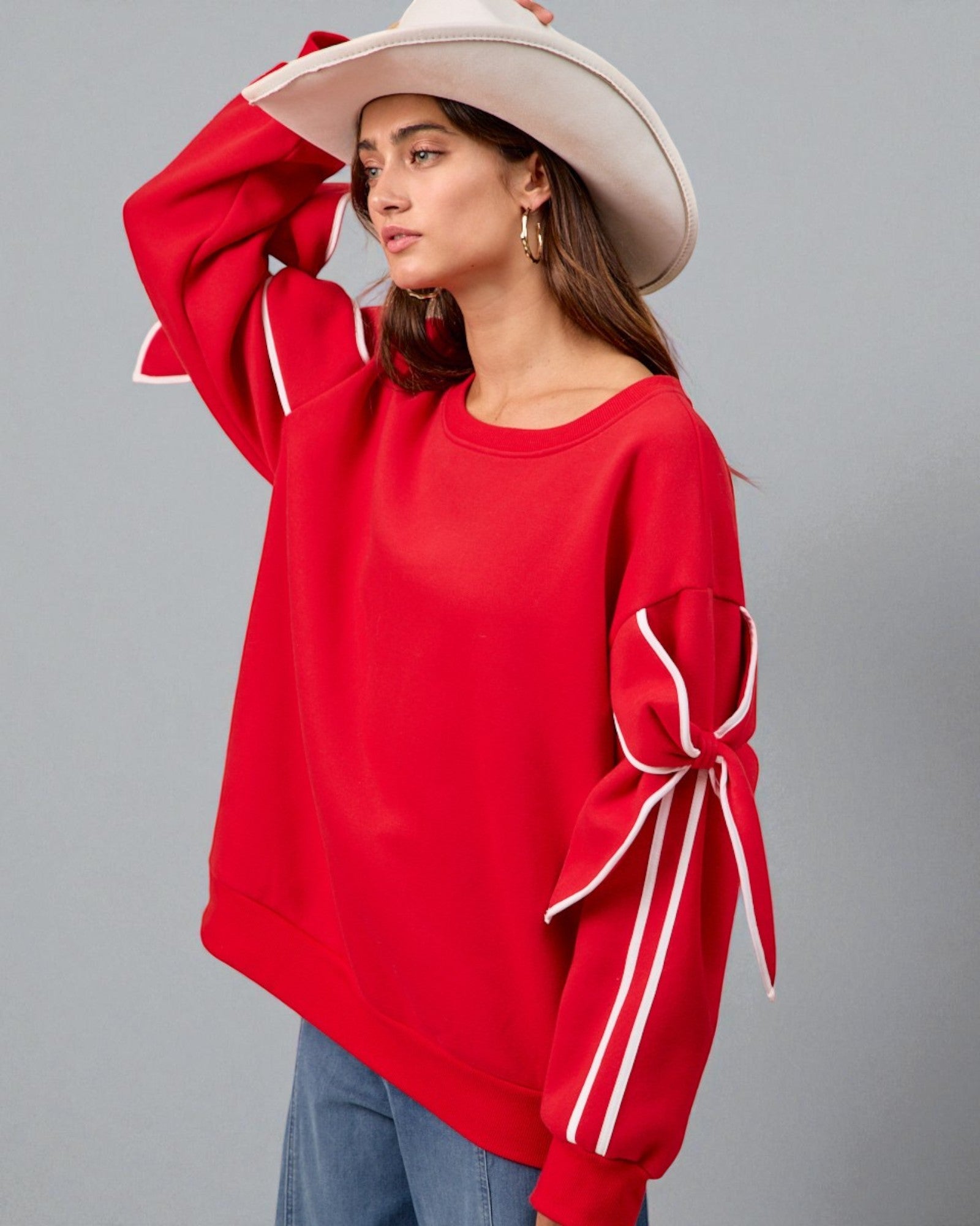 Woman wearing a red sweater with bow details on sleeves against a gray background