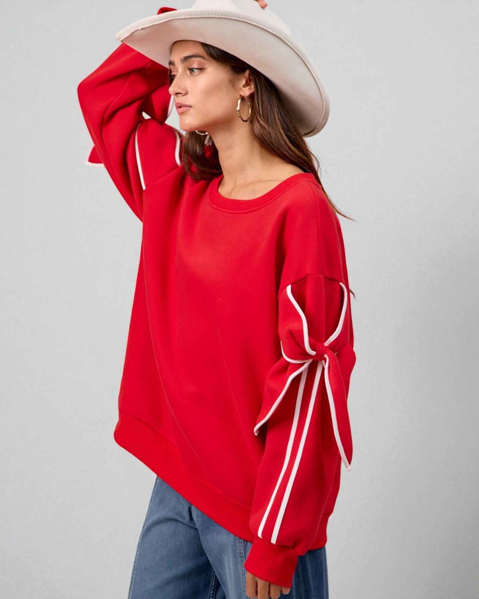 Woman wearing a red sweatshirt with bow details on sleeves against a gray background