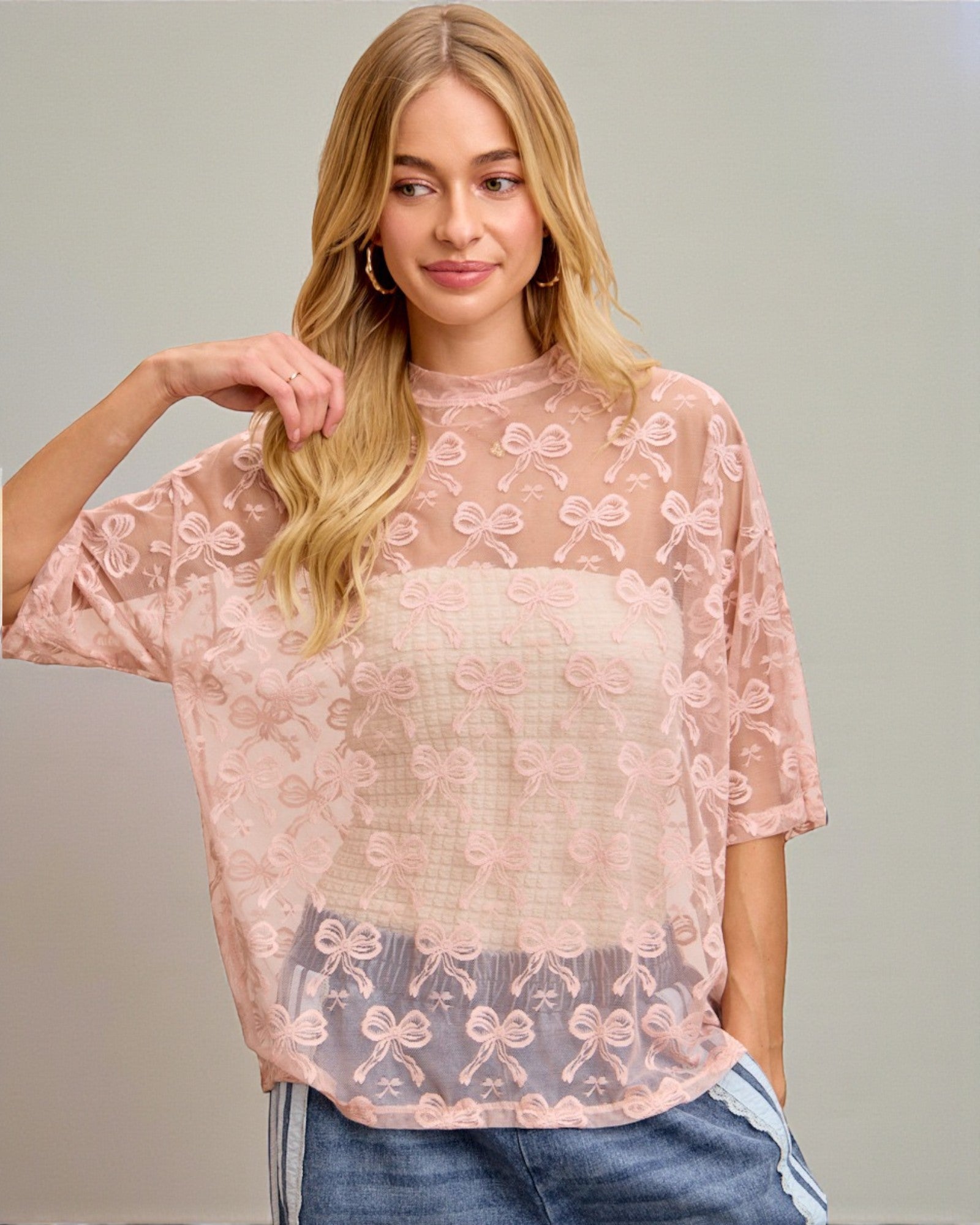 Woman wearing a pink lace top with a plain background