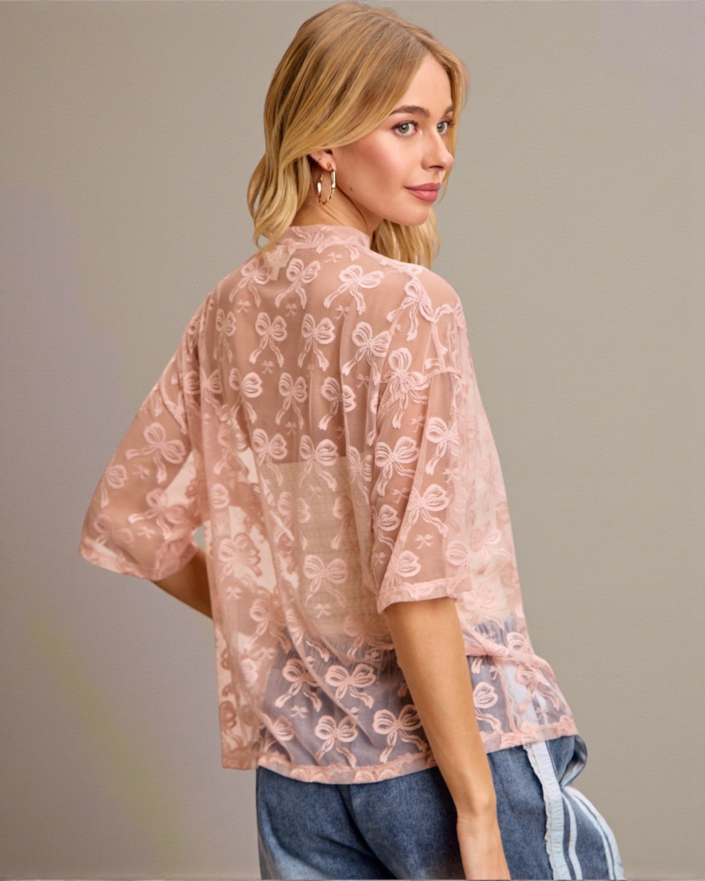 Woman wearing a sheer pink blouse with floral patterns on a plain background