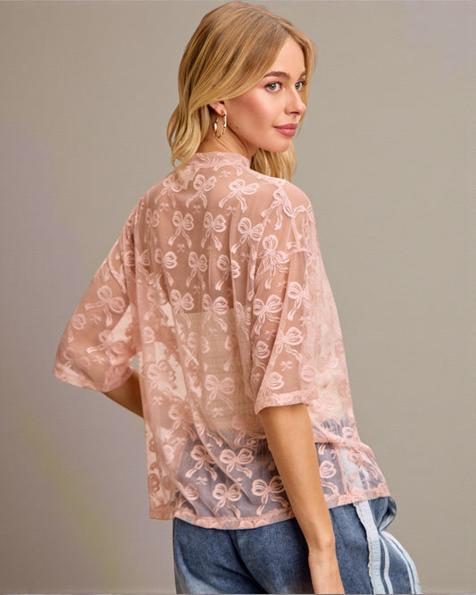 Woman wearing a sheer pink blouse with floral patterns on a plain background