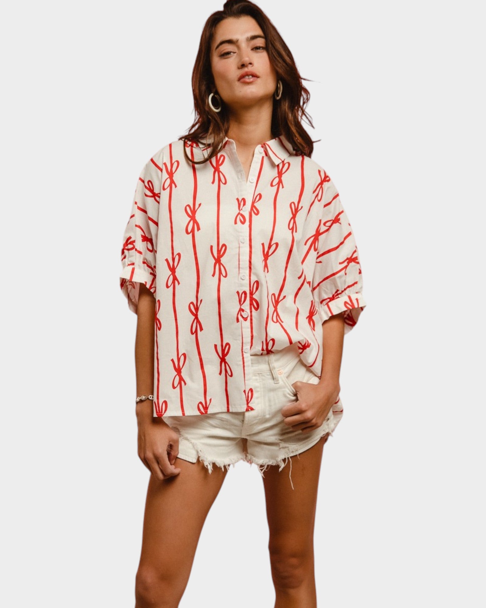 Woman wearing a white blouse with red patterns and denim shorts on a plain background