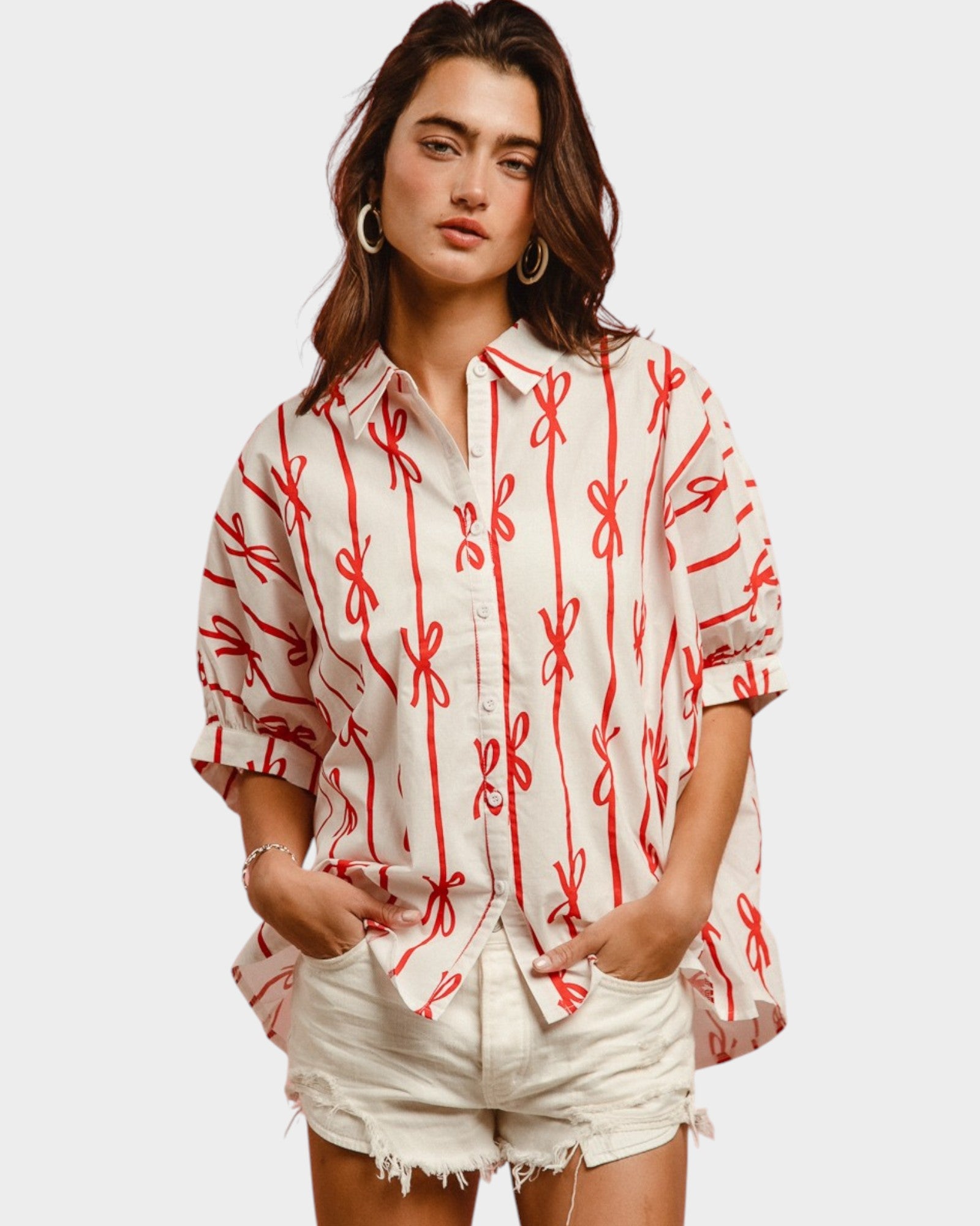 Woman wearing a white shirt with red patterns and white shorts on a plain background