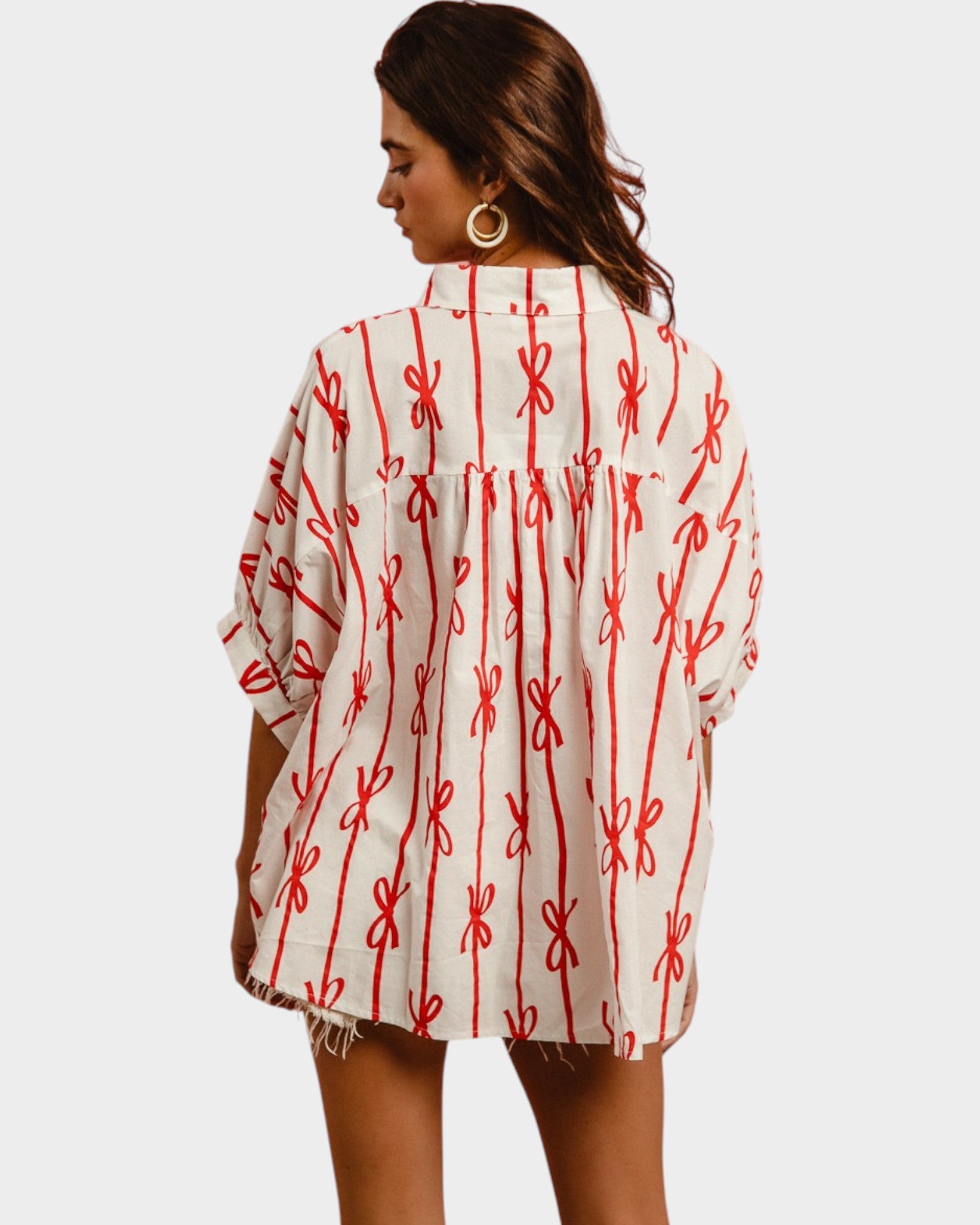 Woman wearing a white shirt with red bow pattern on a plain background