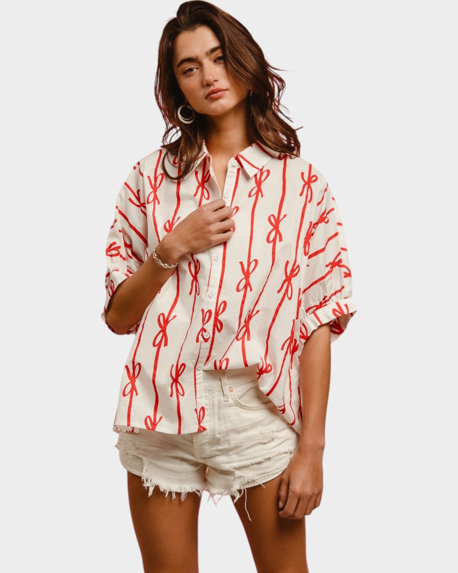 Woman wearing a white blouse with red patterns and white shorts on a plain background