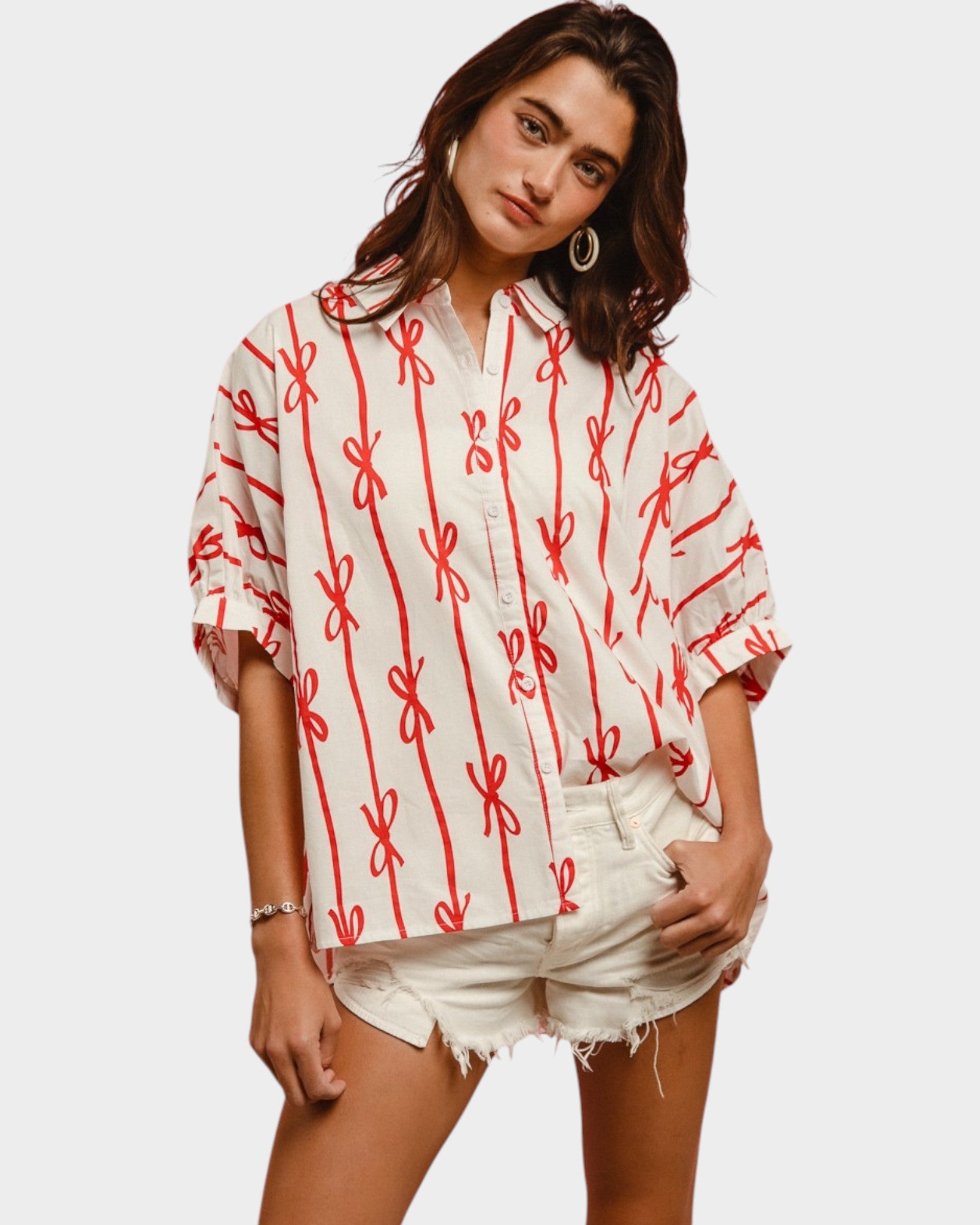 Woman wearing a white blouse with red patterns and white shorts on a plain background