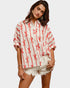 Woman wearing a white blouse with red patterns and white shorts on a plain background