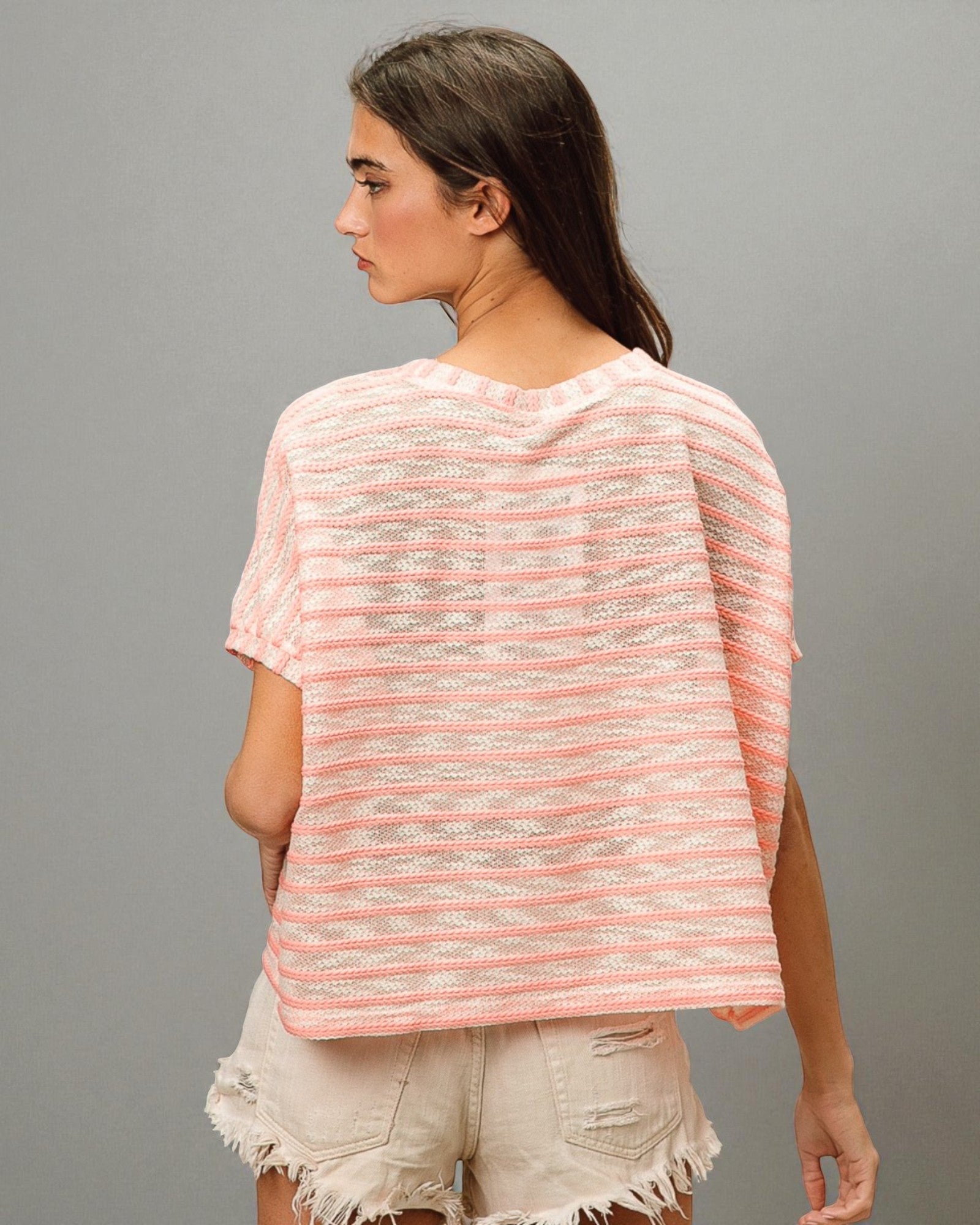 Woman wearing a pink and white striped shirt with beige shorts on a gray background