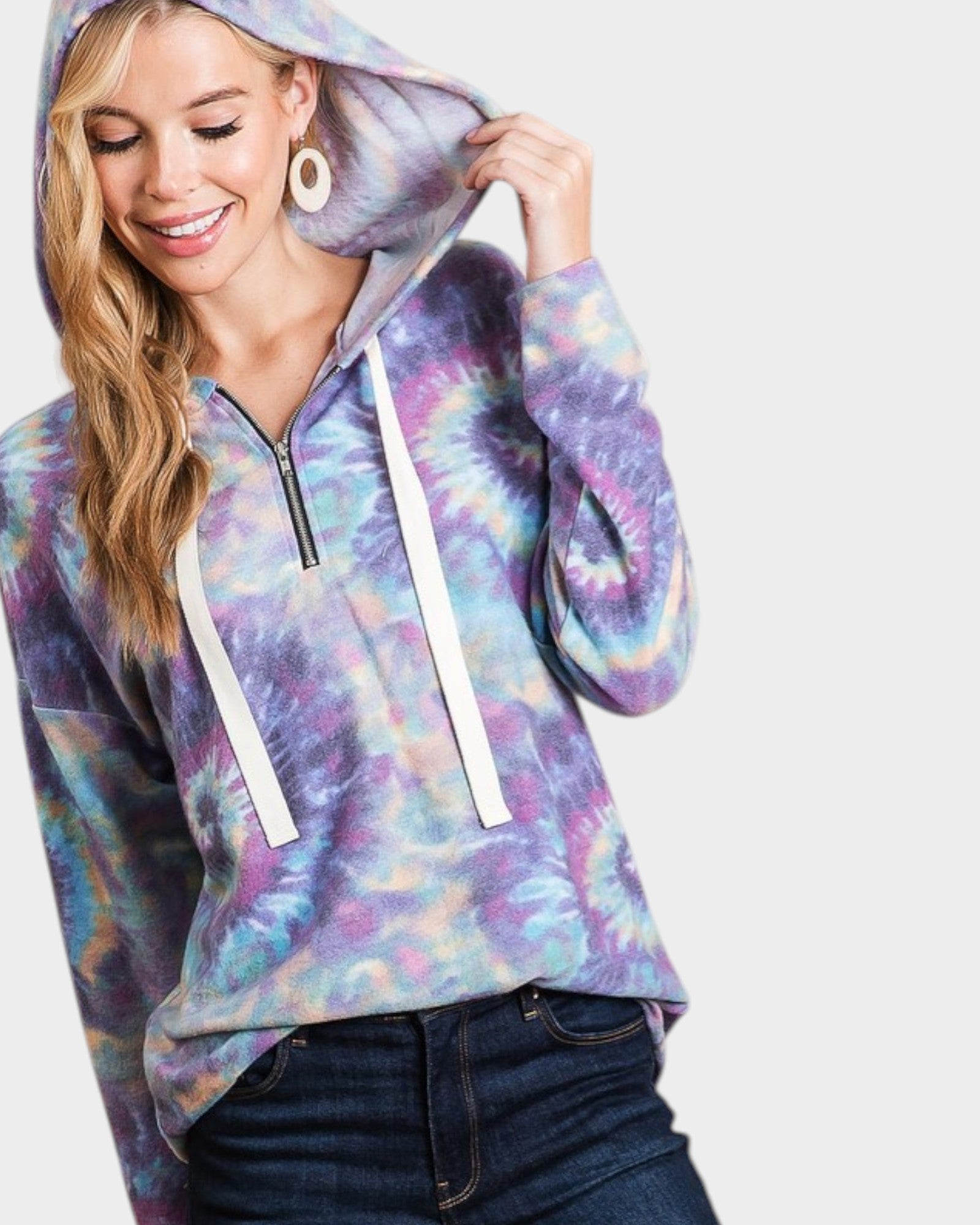 Woman wearing a tie-dye hoodie with a white zipper on a plain background