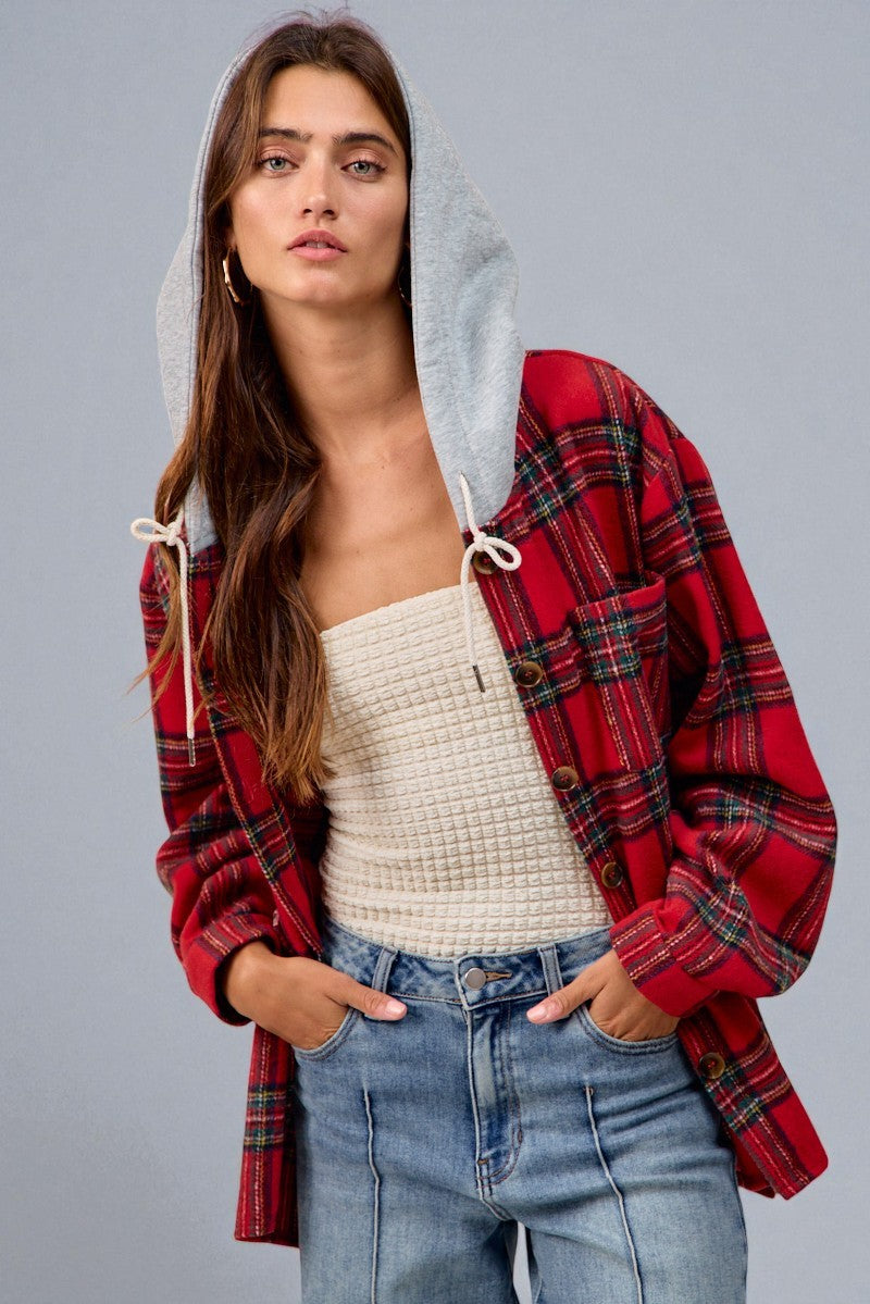 Woman wearing a red plaid shirt with a gray hoodie over a white top and blue jeans on a gray background