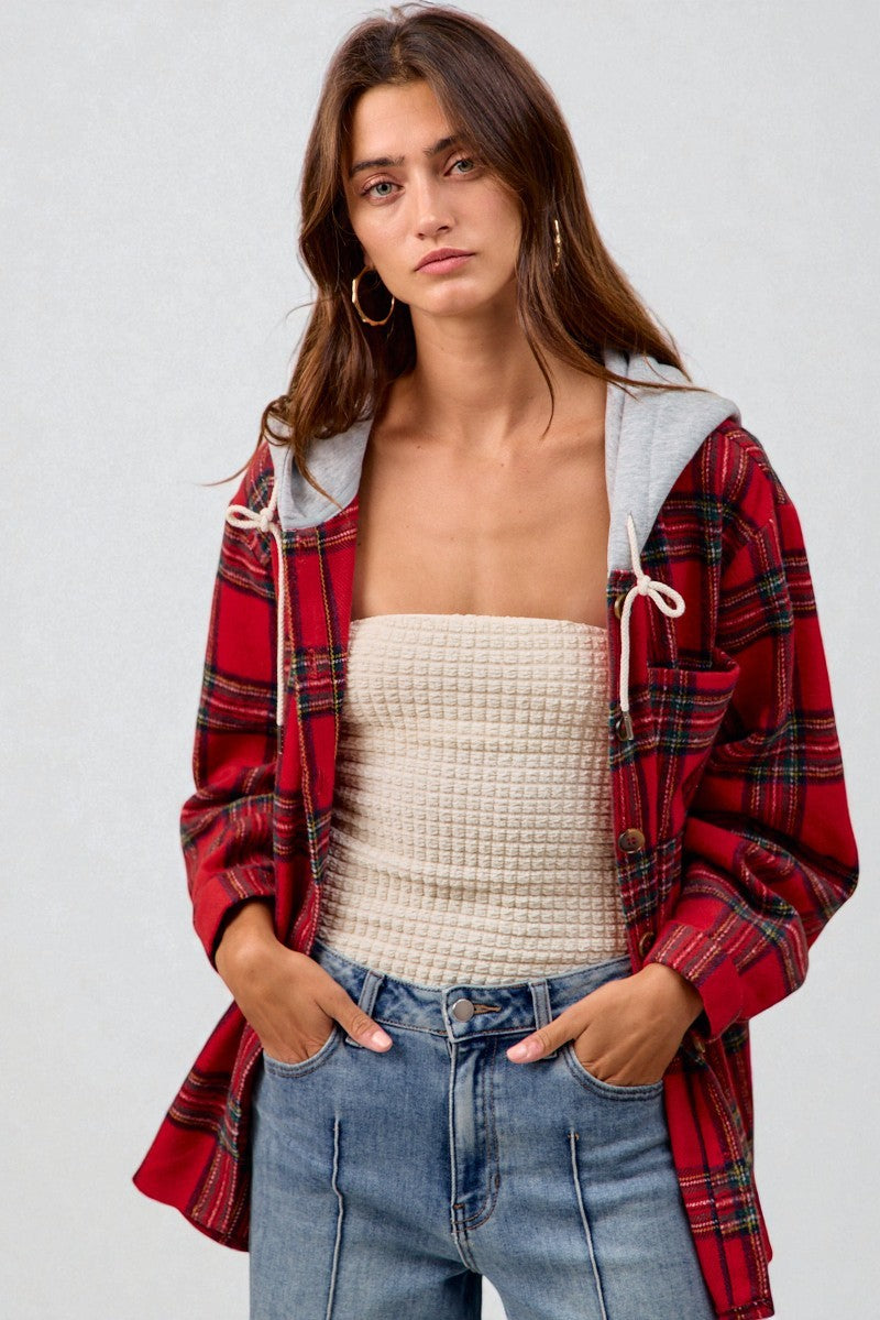 Woman wearing a red plaid shirt over a beige top and blue jeans on a white background