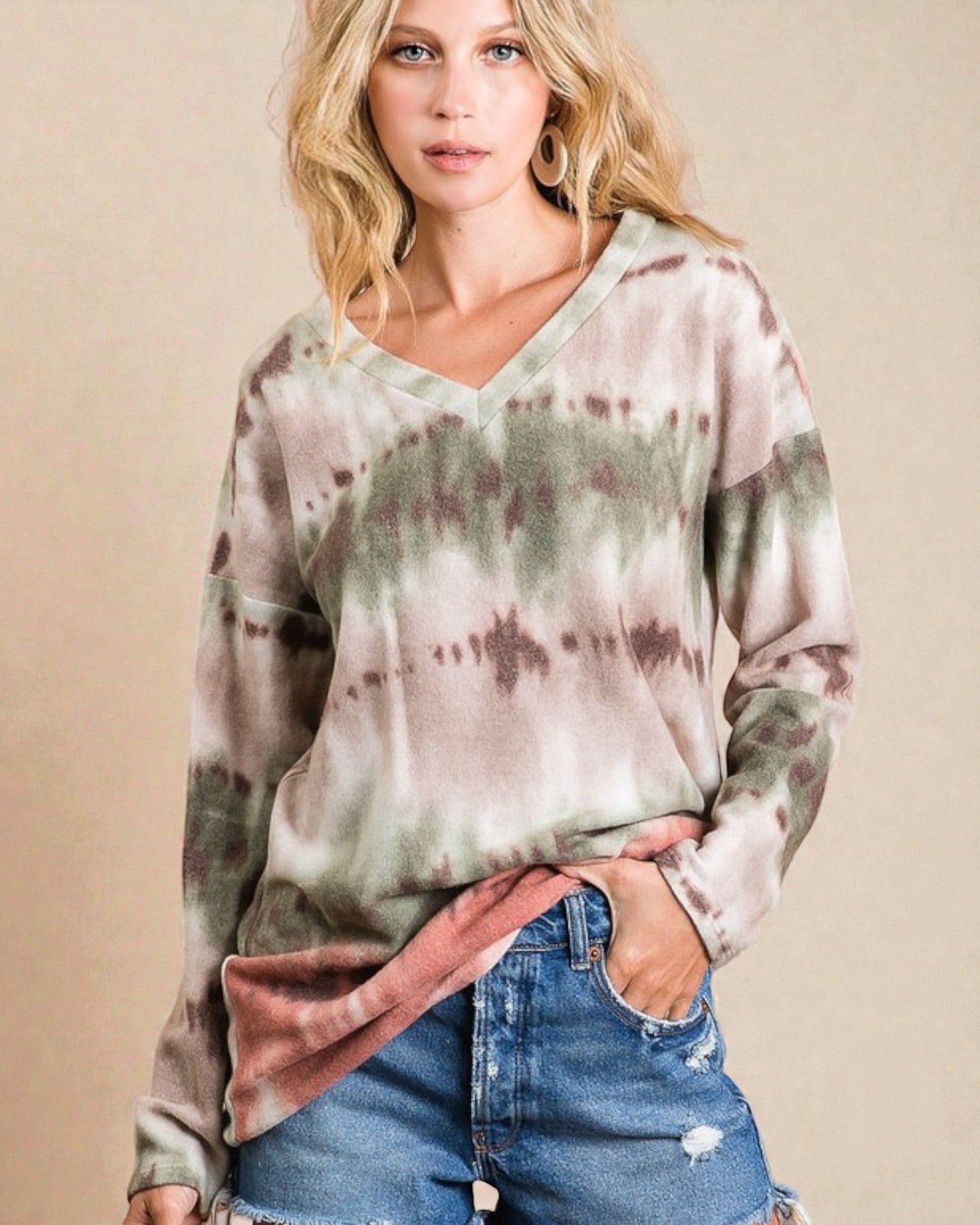 Woman wearing a tie-dye long-sleeve shirt and denim shorts on a beige background