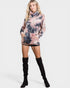 Woman wearing a tie-dye hoodie dress with black knee-high boots on a white background