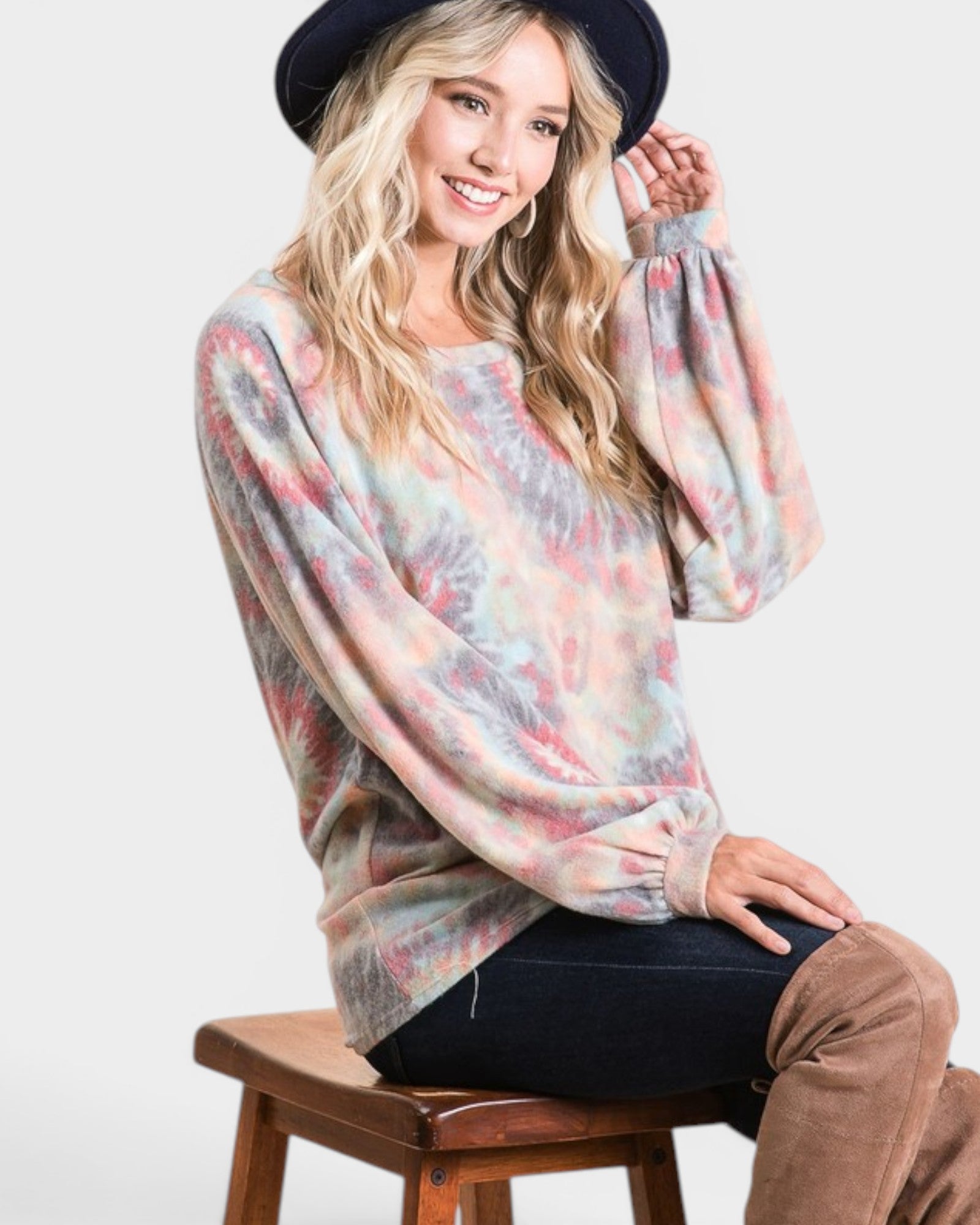 Woman wearing a colorful sweater and black hat sitting on a wooden stool against a white background
