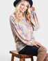Woman wearing a colorful sweater and black hat sitting on a wooden stool against a white background
