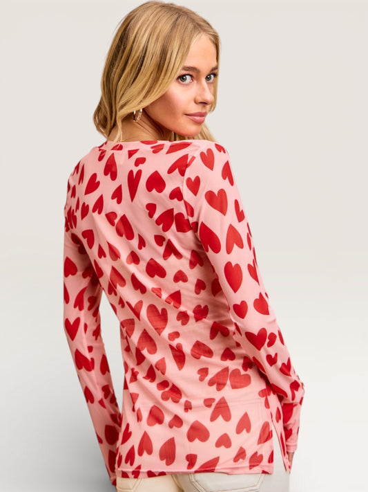 Woman wearing a pink long-sleeve top with red heart patterns on a light gray background