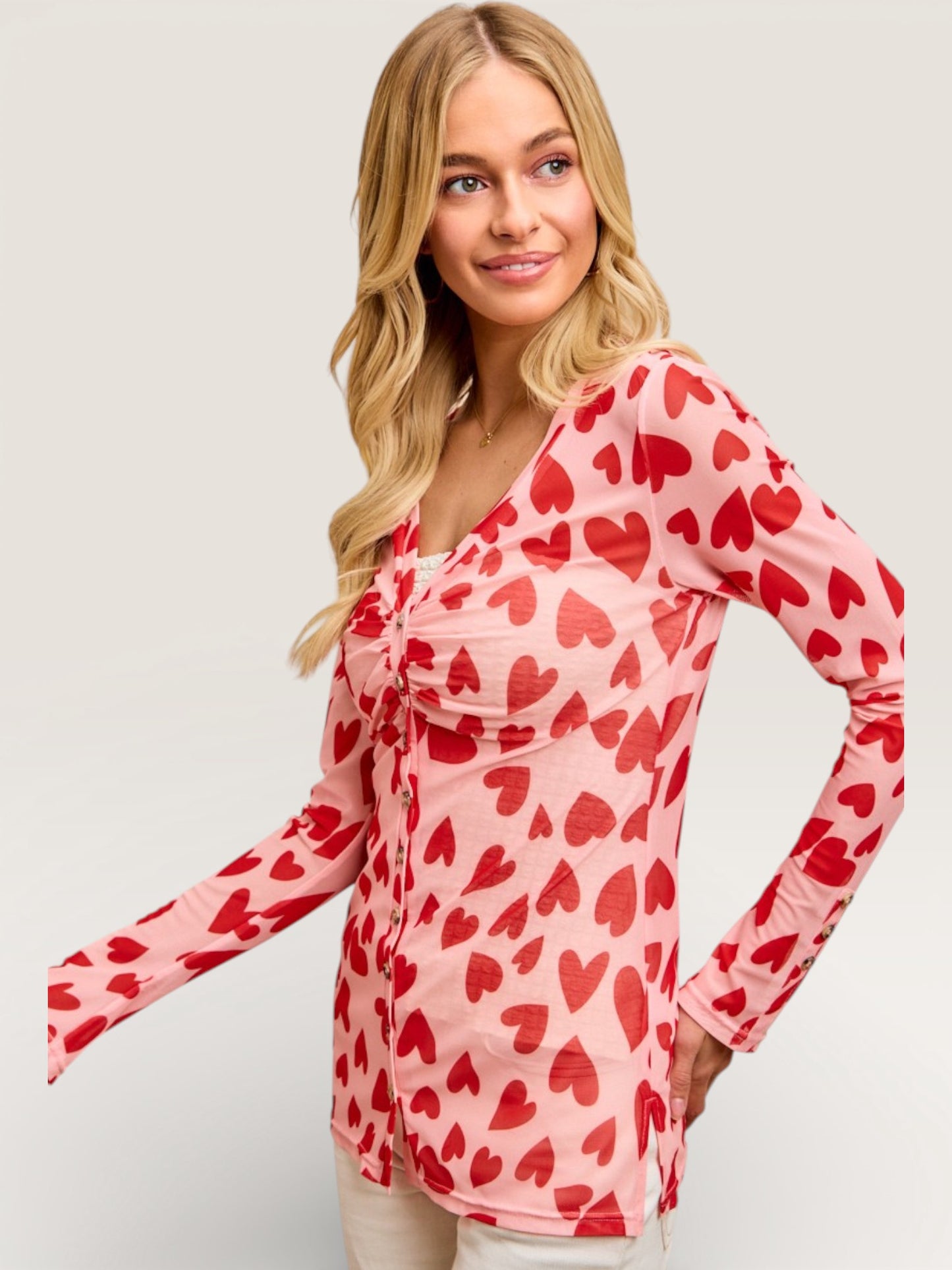 Woman wearing a pink long-sleeve top with red heart patterns on a plain background
