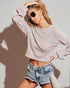 Woman wearing a light pink cropped sweatshirt and denim shorts against a plain background