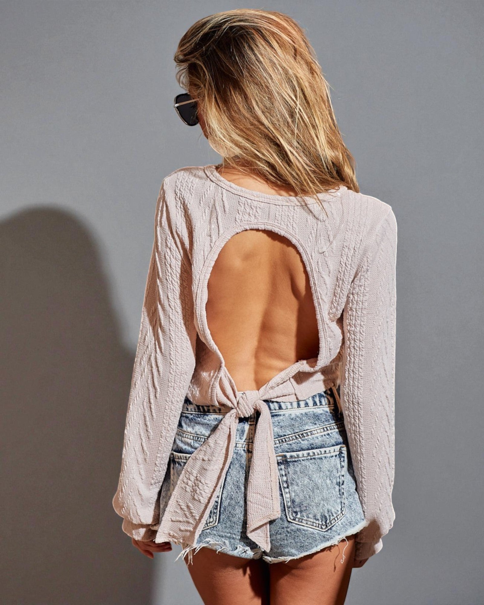 Woman wearing a light pink lace top and denim shorts against a gray background