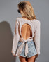 Woman wearing a light pink lace top and denim shorts against a gray background