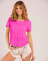 Woman wearing a bright pink textured top and light shorts on a plain background