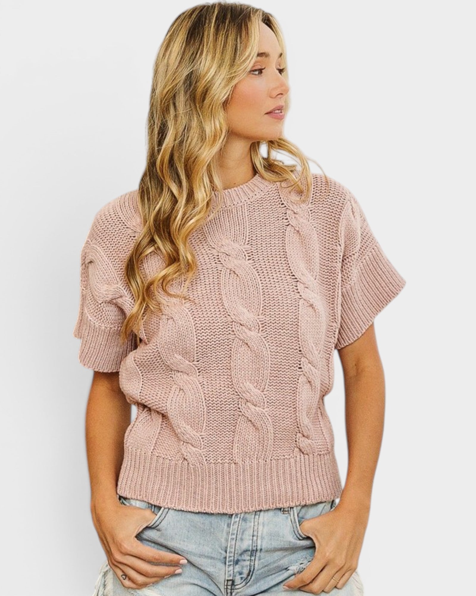 Woman wearing a pink cable knit sweater against a white background