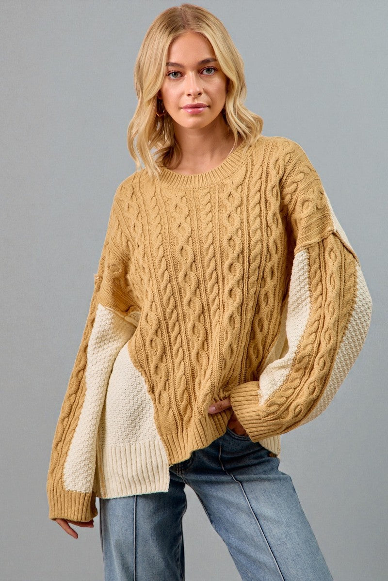 Woman wearing a mustard yellow cable knit sweater with white sleeves against a gray background