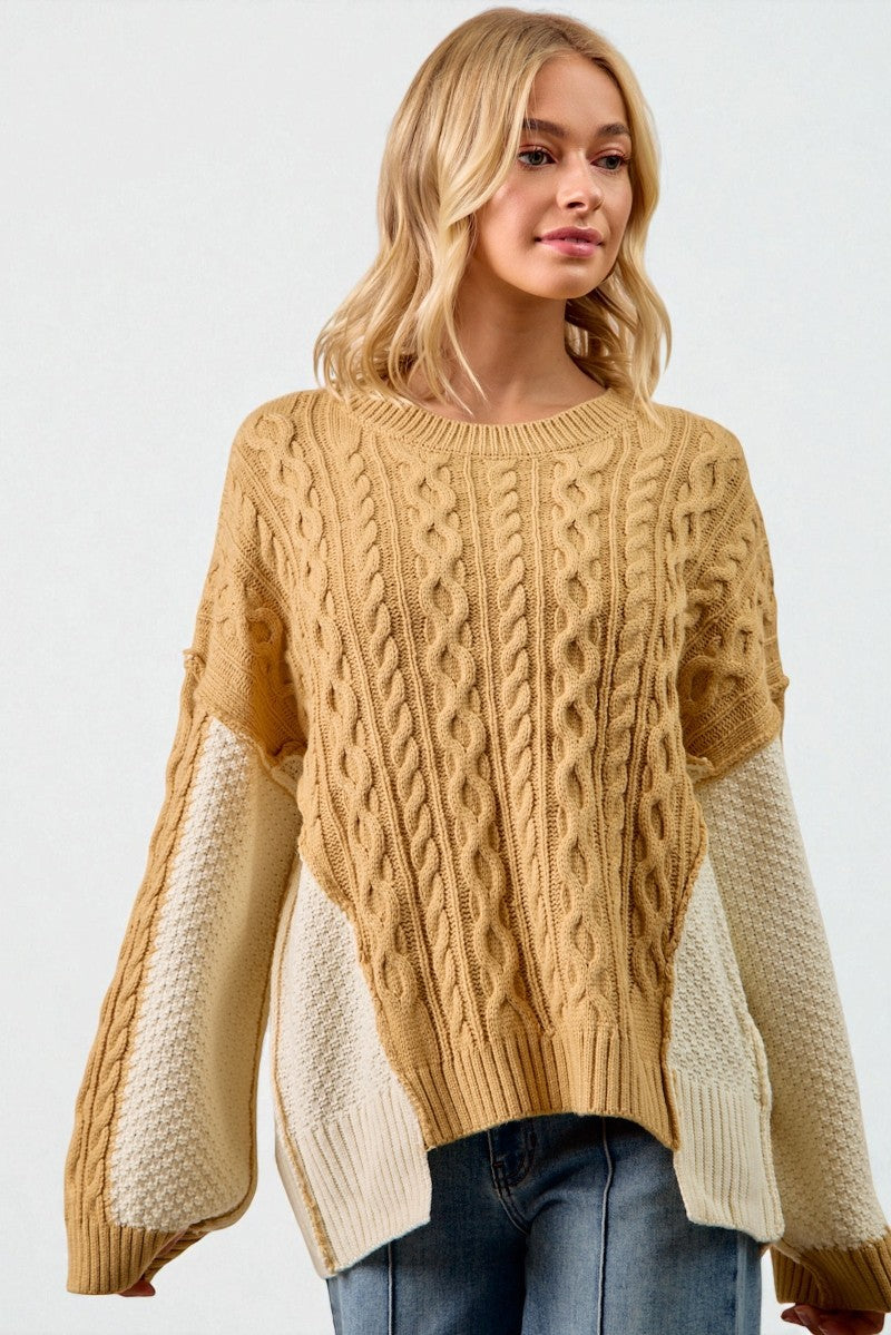 Woman wearing a beige cable knit sweater with white sleeves on a plain background