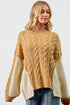 Woman wearing a beige cable knit sweater with white sleeves on a plain background