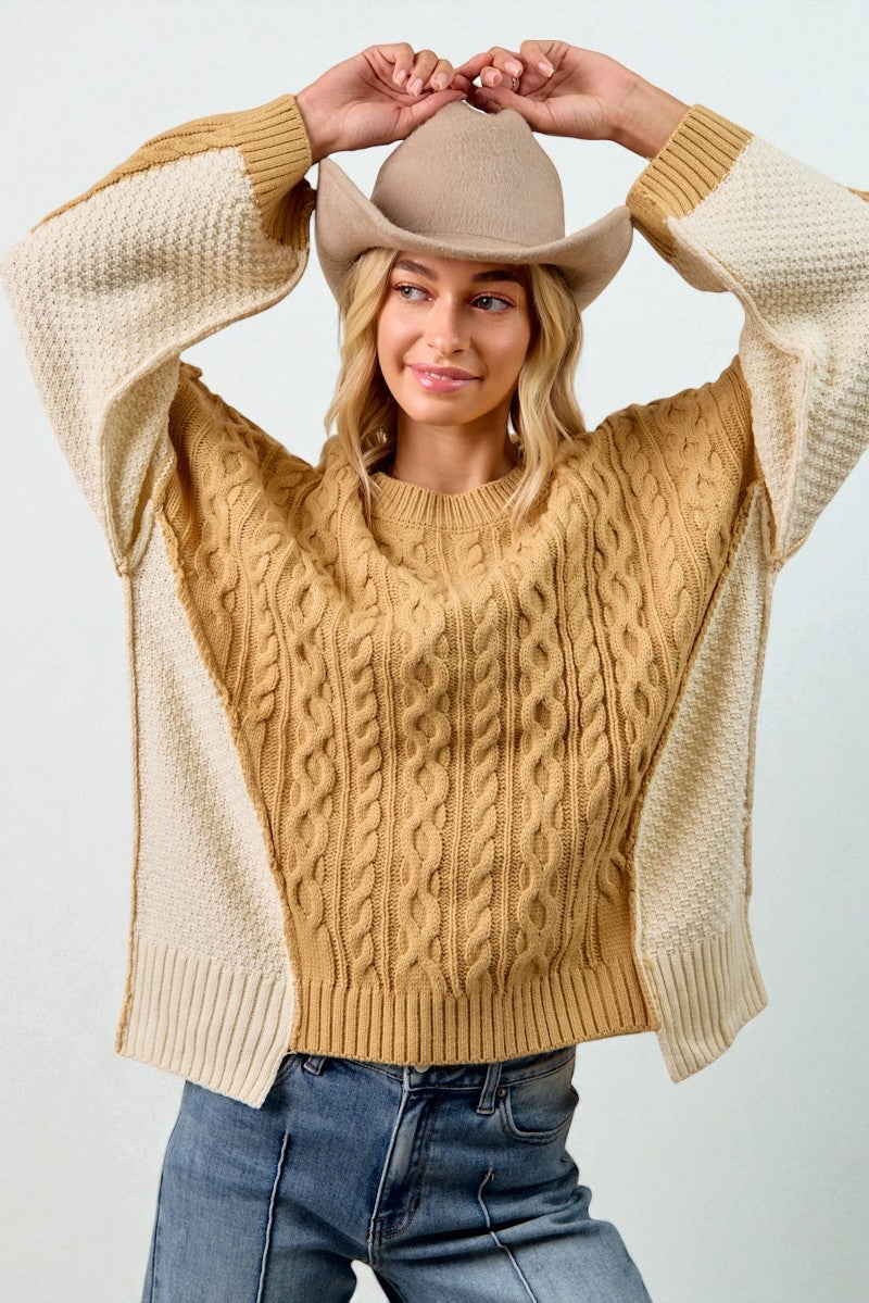 Woman wearing a beige cable knit sweater and a beige cowboy hat against a white background