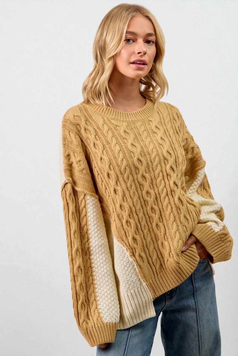 Woman wearing a mustard yellow cable knit sweater over a cream sweater with blue jeans on a white background