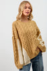 Woman wearing a mustard yellow cable knit sweater over a cream sweater with blue jeans on a white background