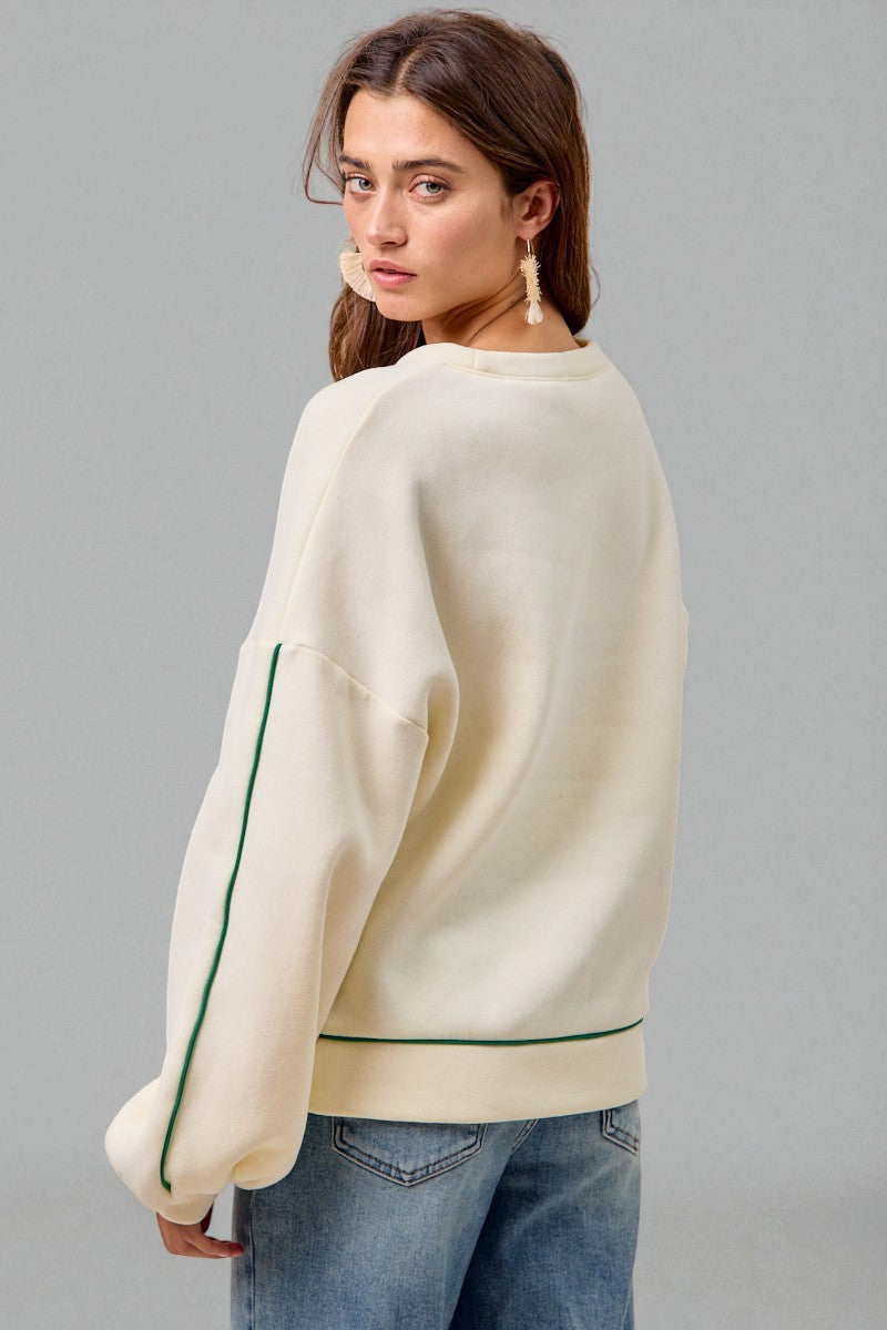 Woman wearing a cream sweater with green accents on a gray background