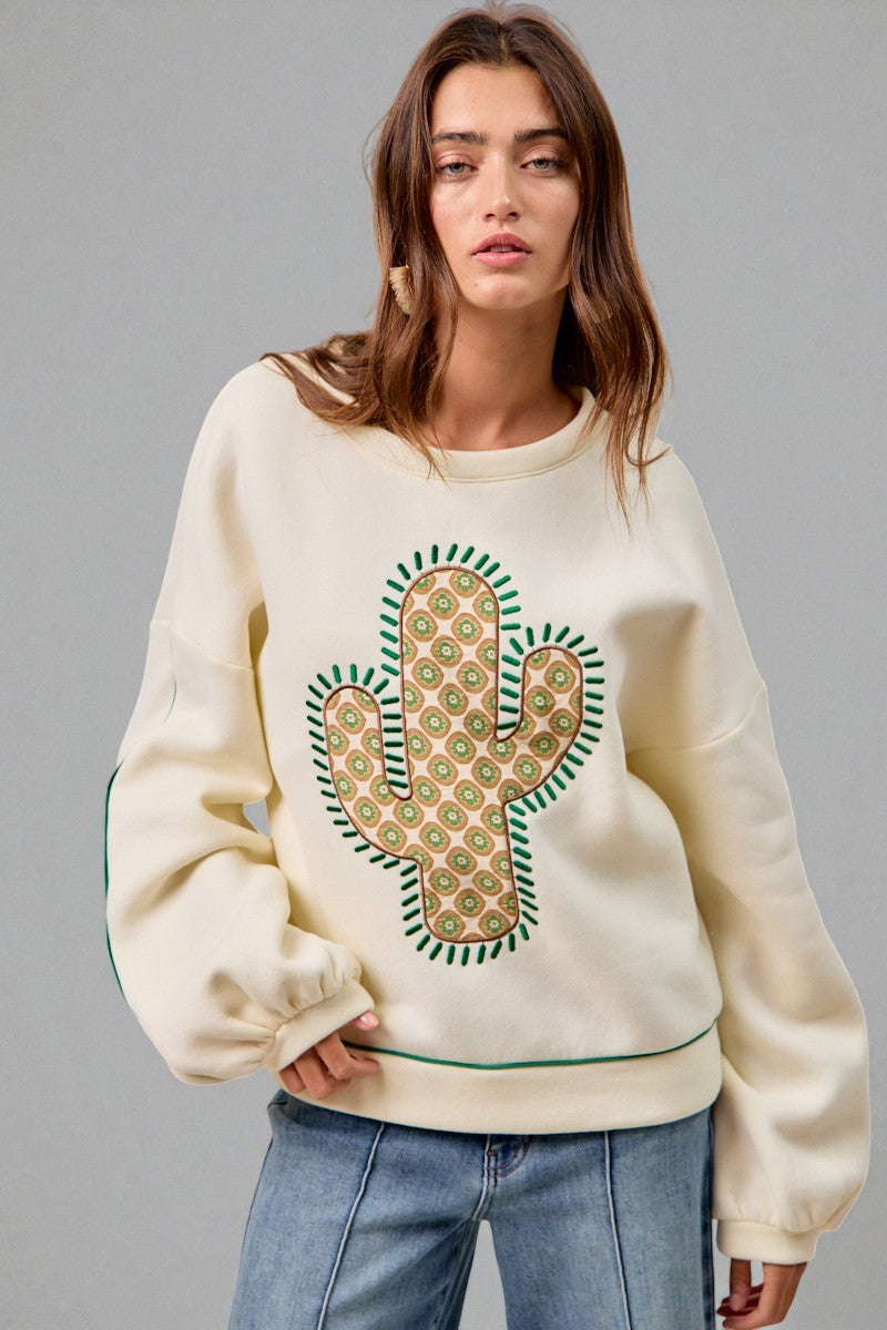Woman wearing a cream sweatshirt with a cactus design on a gray background