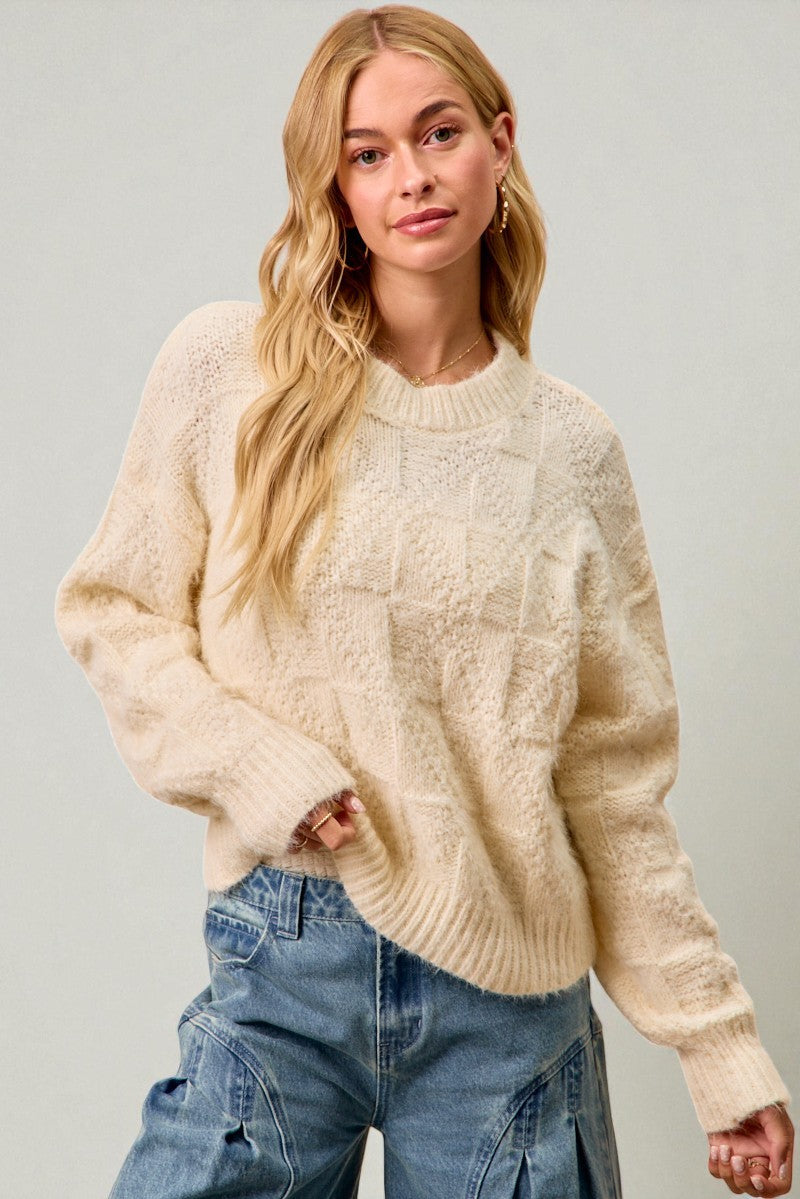 Woman wearing a cream sweater and blue jeans against a plain background