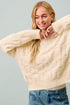Woman wearing a cream sweater and blue jeans against a light gray background