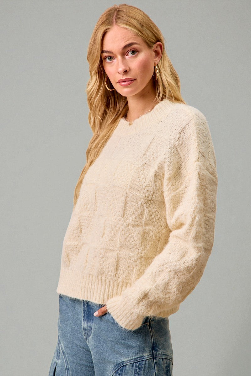 Woman wearing a cream sweater and blue jeans against a gray background