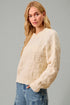 Woman wearing a cream sweater and blue jeans against a gray background